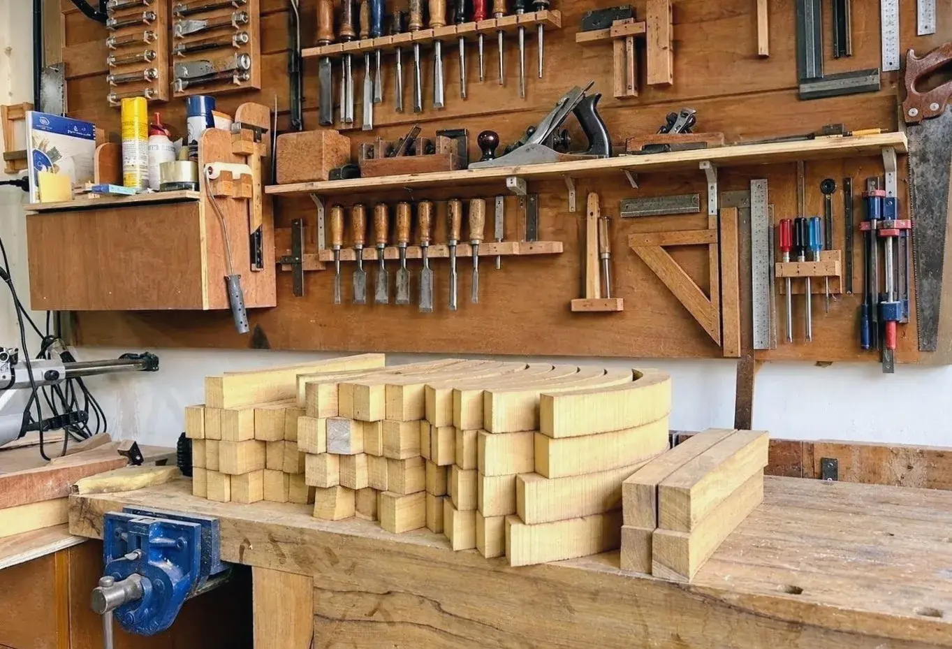 Hand tools on the workshop wall above a bench stacked with cut timber